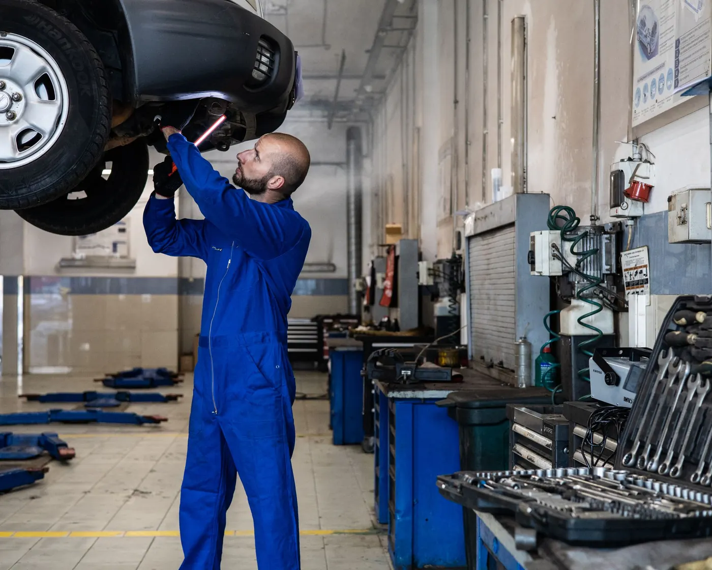 A mechanic inspecting a car on a lift in a service garage